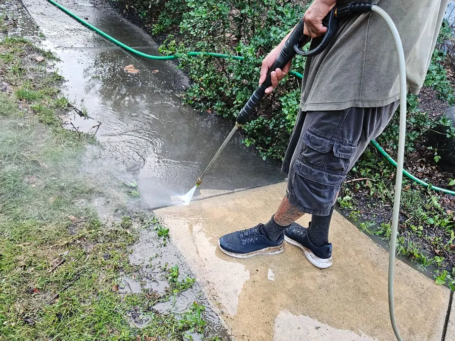 Pressure washing a concrete walkway, with the cleaned section visibly brighter
